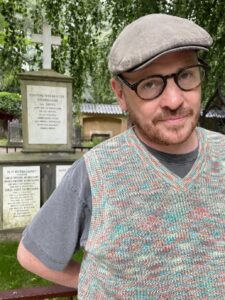 Portrait photo of Conor wearing a cap and glasses, standing in front of a memorial.