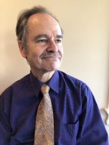 Portrait photo of Jon wearing a dark indigo shirt and paisley tie